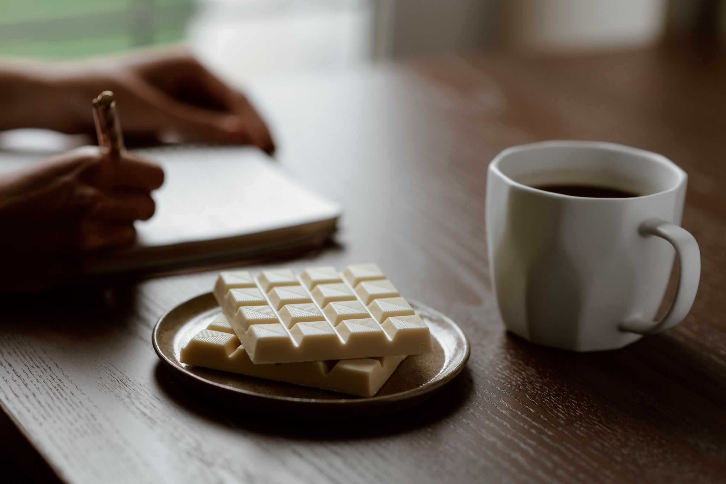 A person writing in a notebook beside a cup of coffee