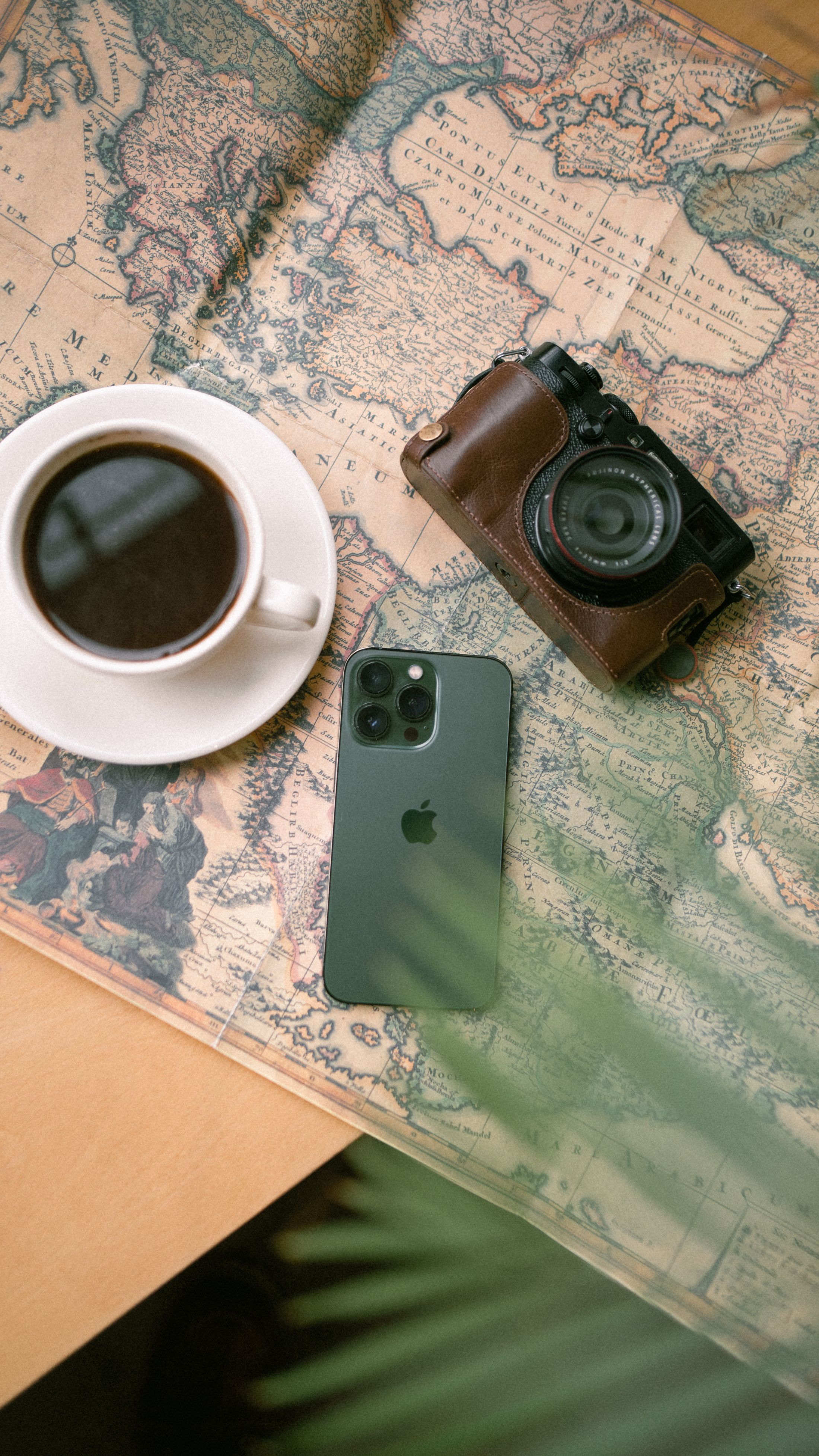 A phone, camera, and cup of coffee arranged on a vintage world map